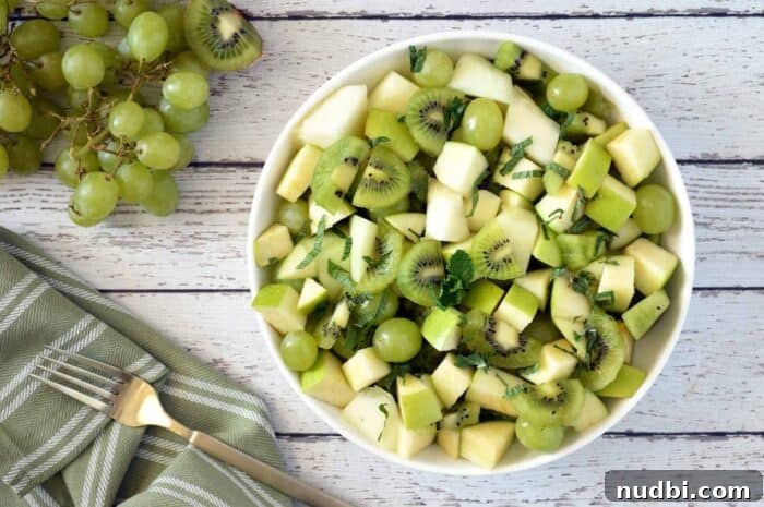 Green fruit salad in white bowl with grapes, kiwi, and honeydew on a whitewashed wooden table