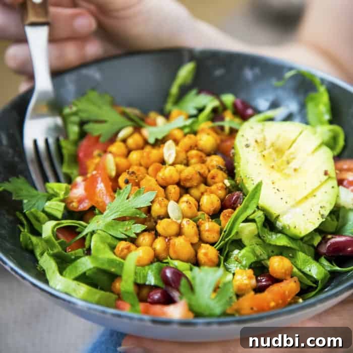 Fork digging into a buddha bowl full of fresh greens, tomatoes, chickpeas, olives and avocado