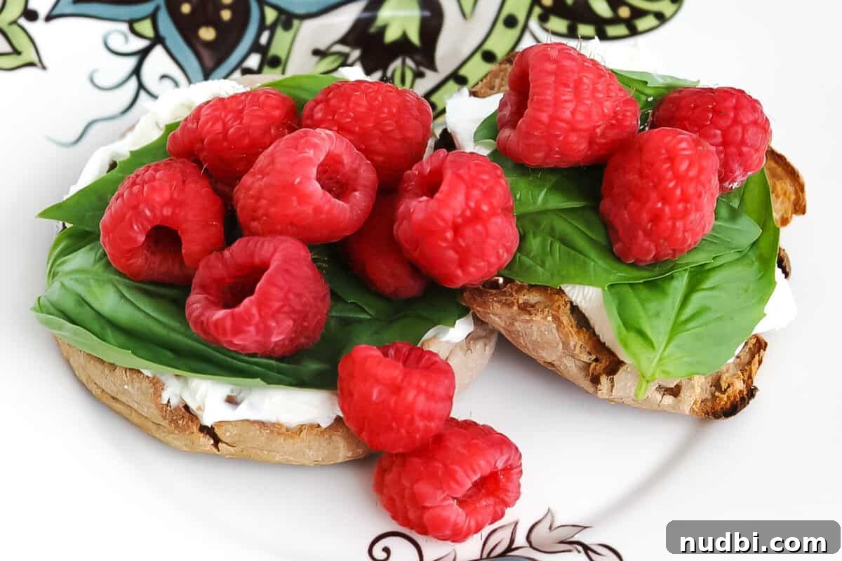 Effortless English Muffin Breakfast Solutions 4 Close-up of a delectable English muffin topped with fresh raspberries, vibrant basil, and creamy cream cheese, ready to be enjoyed.