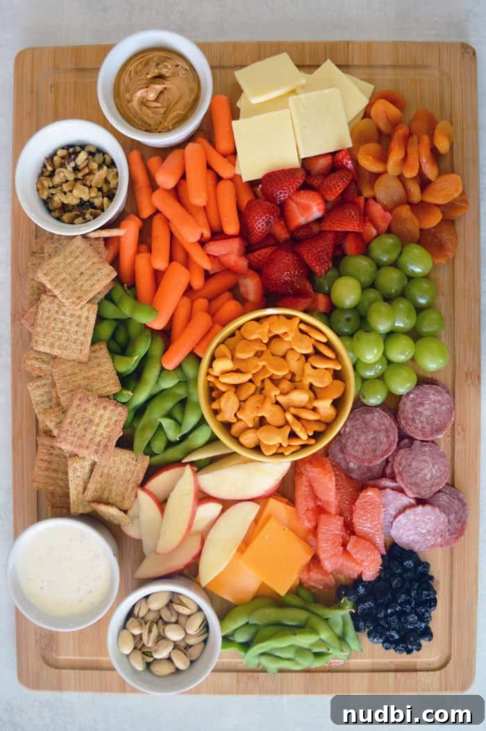 Overhead view of a vibrant, colorful family snack board filled with fruits, vegetables, cheeses, and crackers.
