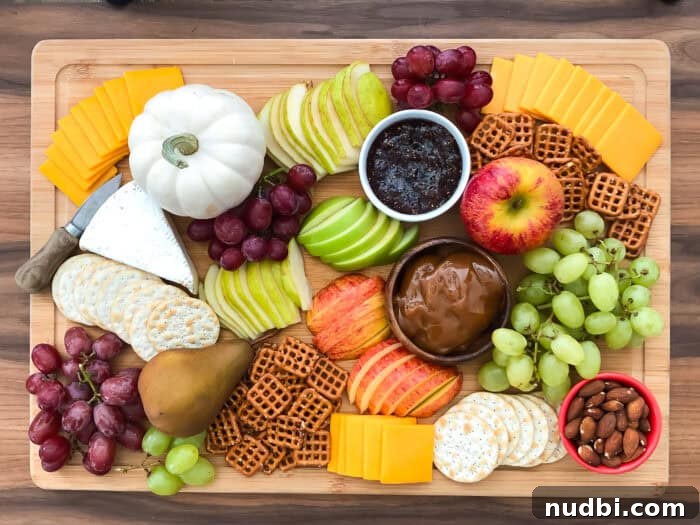 A vibrant Fall Harvest Snack Board filled with red and green apples, pears, grapes, cheese, and crackers, perfect for a healthy Thanksgiving appetizer.