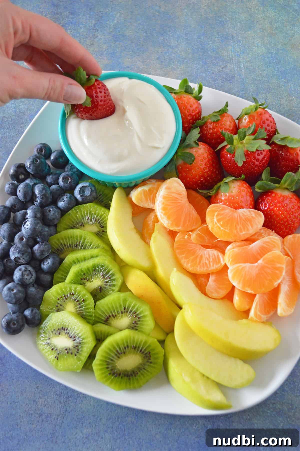 10 Creative Ways to Pack More Fruits and Veggies in Kids' Lunchboxes 2 A hand dipping a fresh strawberry into a creamy, delicious cream cheese fruit dip, highlighting a fun way to eat fruit.