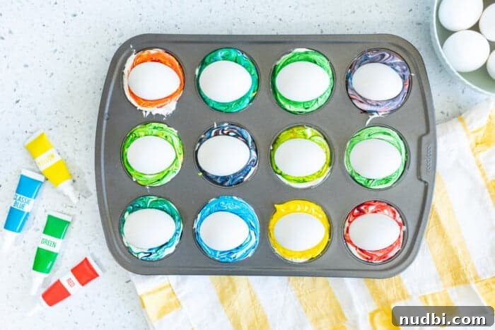 A child's hands carefully swirl blue and purple food coloring into a dollop of Cool Whip in a muffin tin section.