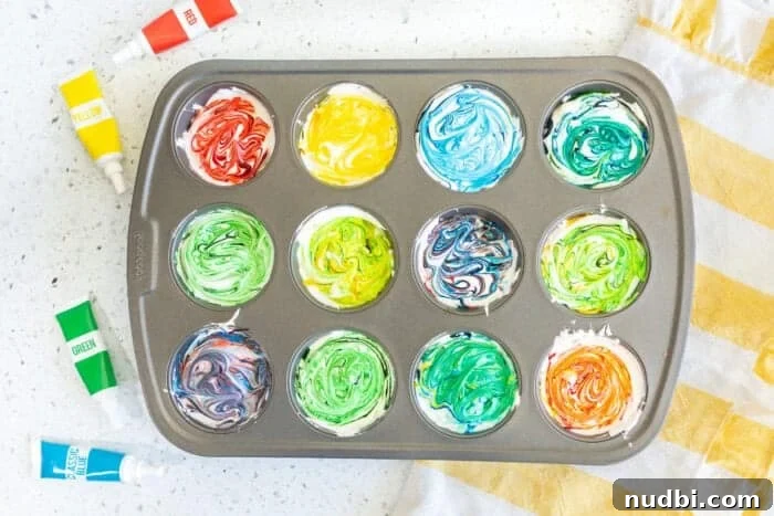 Close-up of a muffin tin filled with dollops of Cool Whip, each with drops of different gel food colorings before swirling.