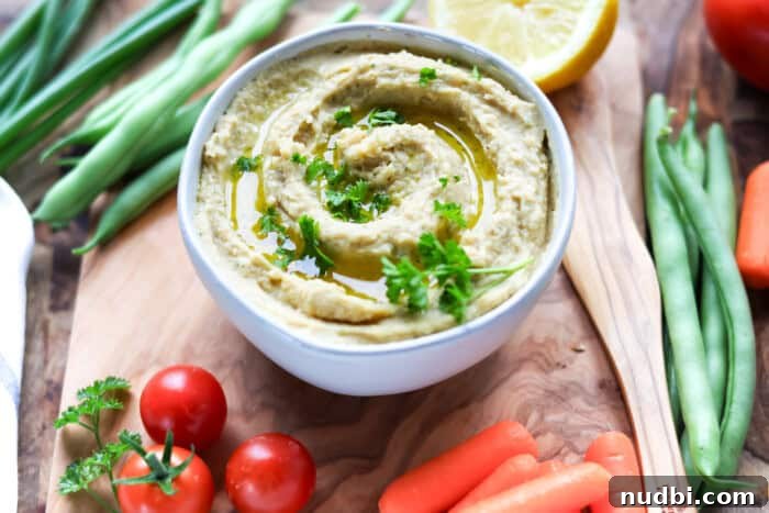 A bowl of creamy homemade Ranch Hummus Dip, garnished with fresh dill, served with a variety of colorful vegetable sticks and pita bread.