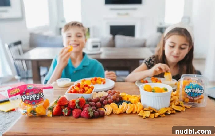 Two cheerful children enjoy a vibrant back-to-school snack board featuring Sunset® Sprinkles tomatoes, Peppy's tiny peppers, fresh strawberries, juicy grapes, sweet clementines, and crunchy crackers on a rustic wooden board in a brightly lit kitchen.
