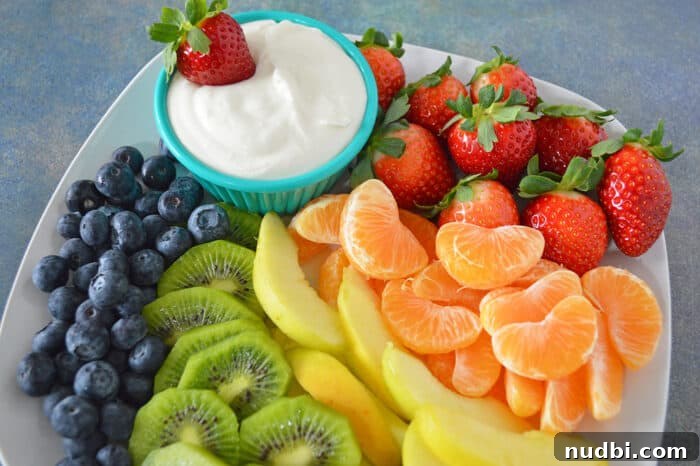 Cream cheese fruit dip in bowl plated with blueberries, kiwi, yellow apples, mandarins and strawberries.
