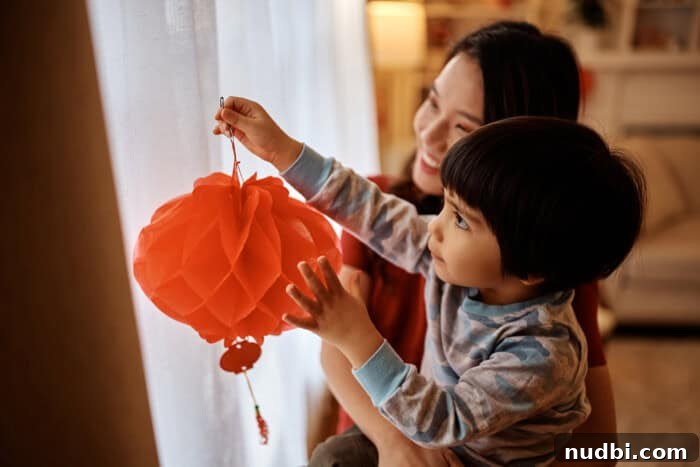 Chinese boy hanging vibrant red lanterns on a window with his mother, symbolizing good fortune for Lunar New Year.