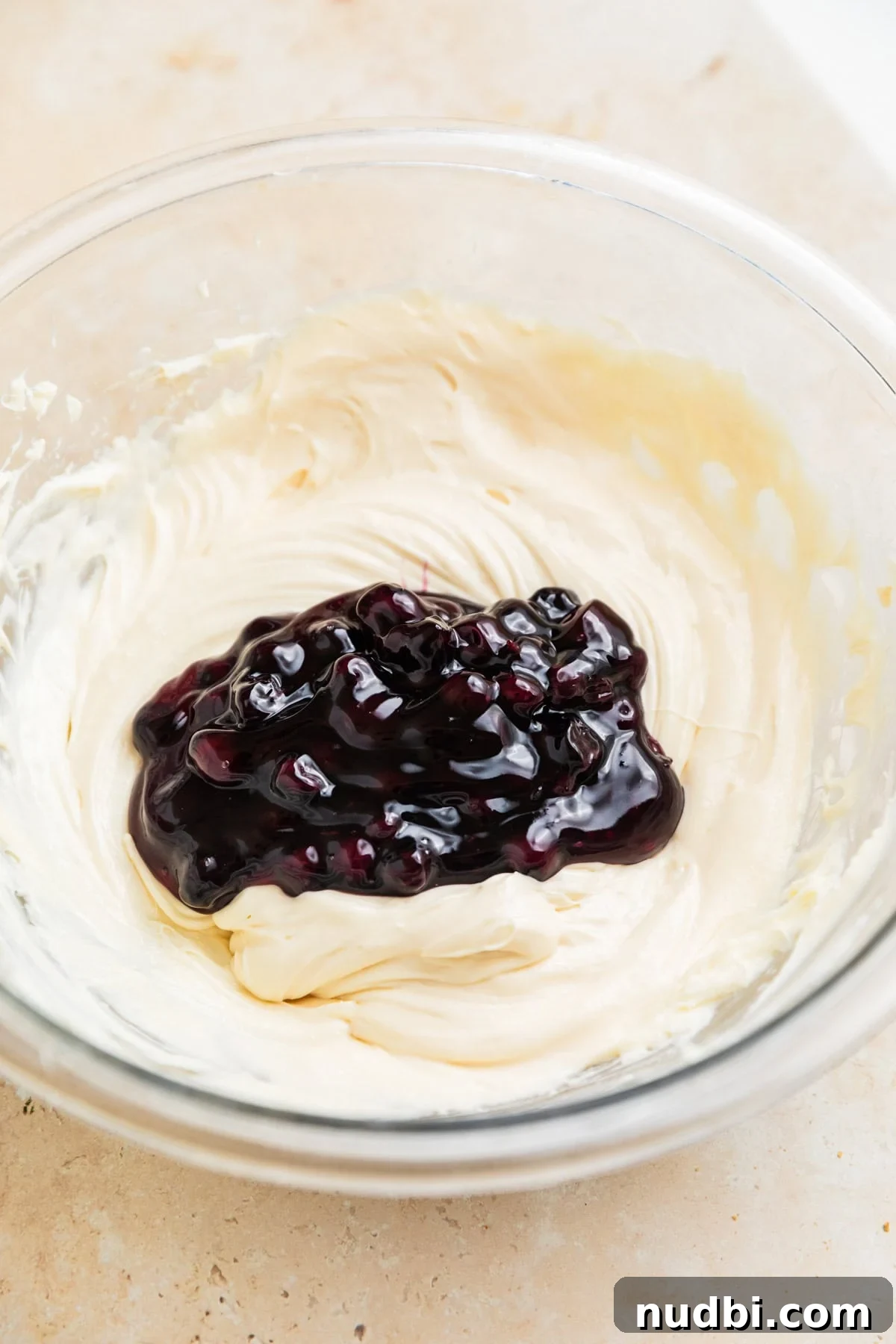 Creamy Blueberry Cheesecake Dip Recipe for Fruit & Crackers 6 Blueberry pie filling added to cheesecake dip mixture in glass bowl.