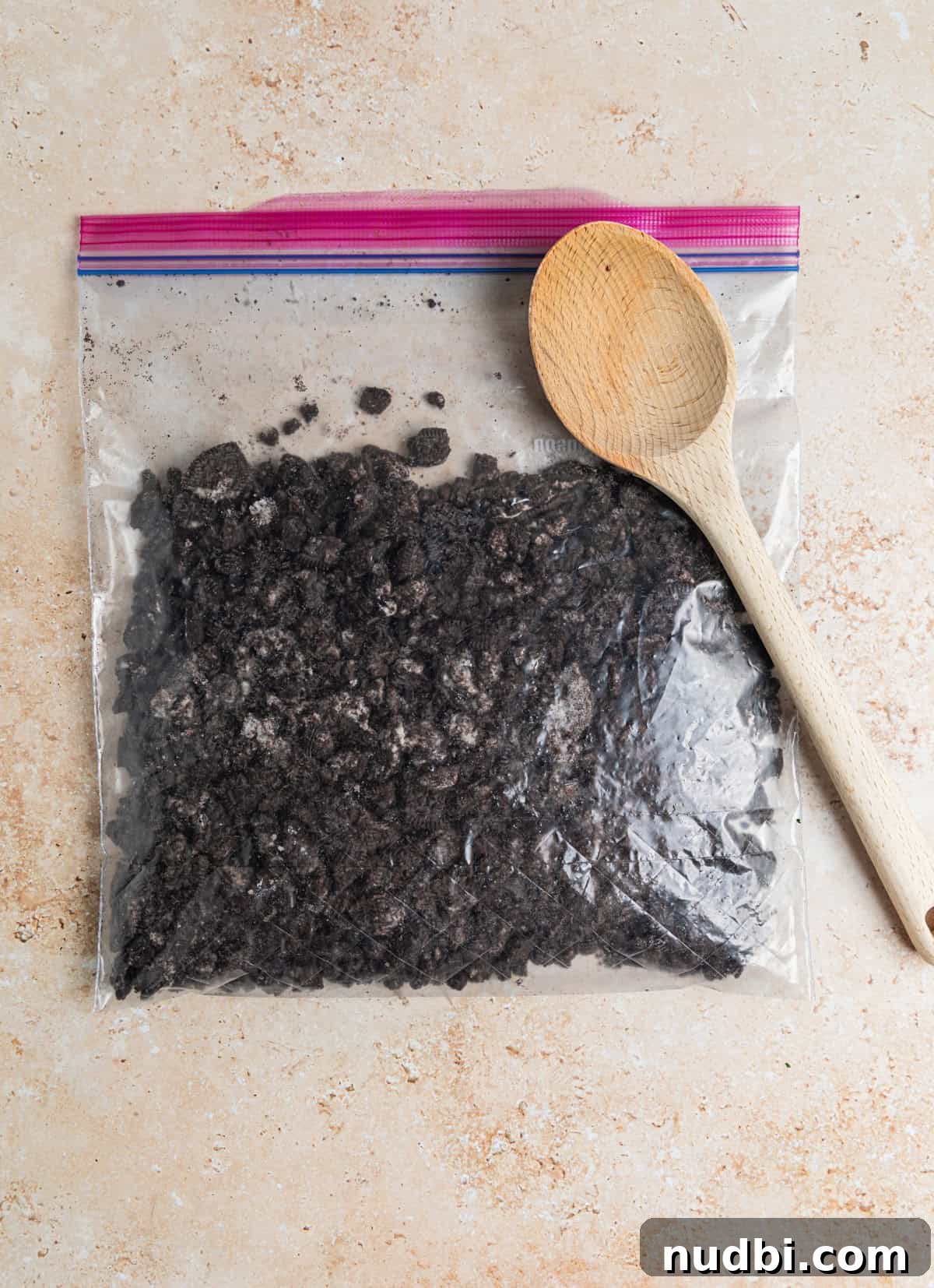 No-Bake Oreo Cheesecake Cups Recipe for Creamy Dessert 5 Crushed Oreos in plastic bag with wooden spoon set on top.