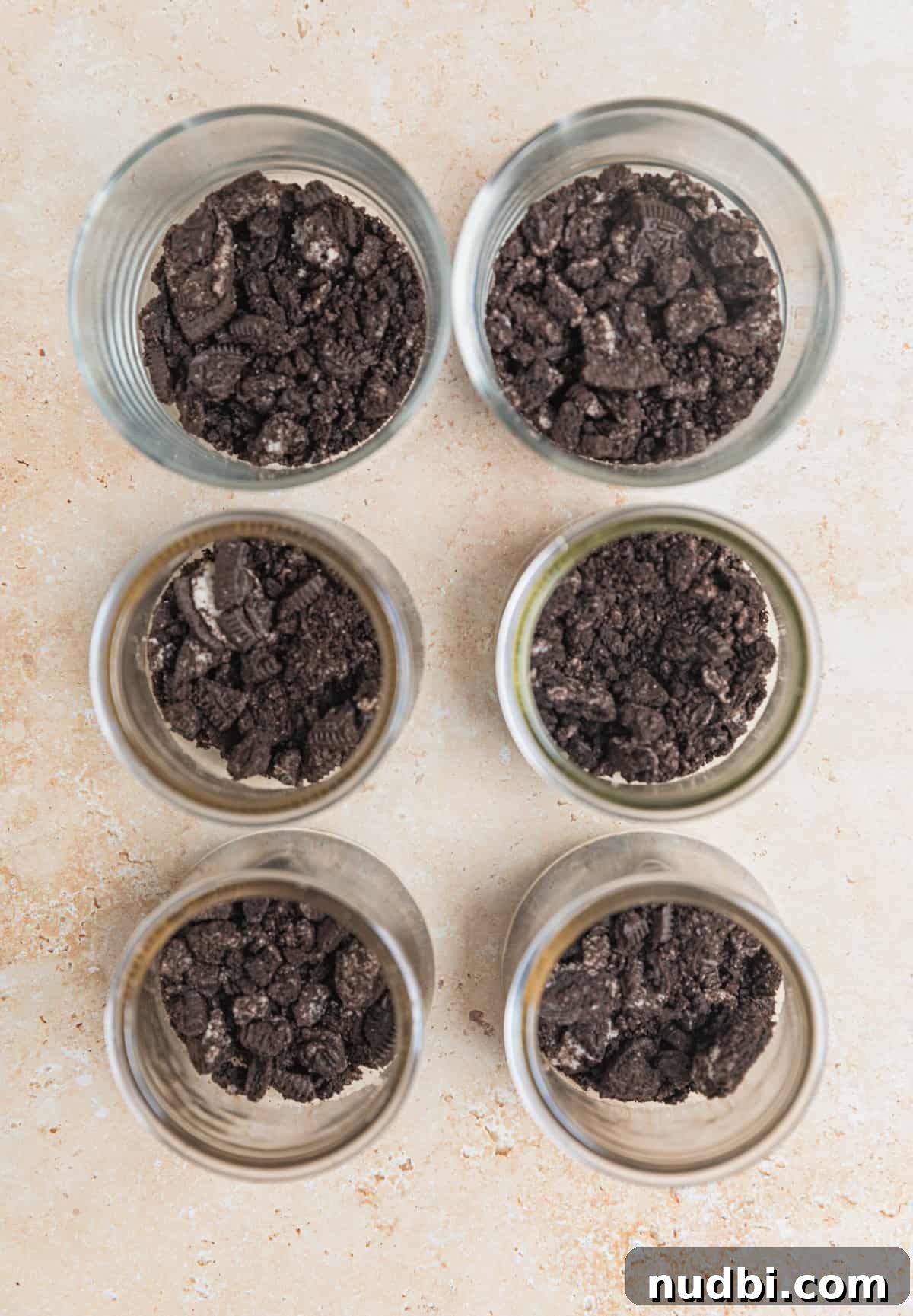 No-Bake Oreo Cheesecake Cups Recipe for Creamy Dessert 6 Crushed Oreos in bottom of 6 glass dessert jars.