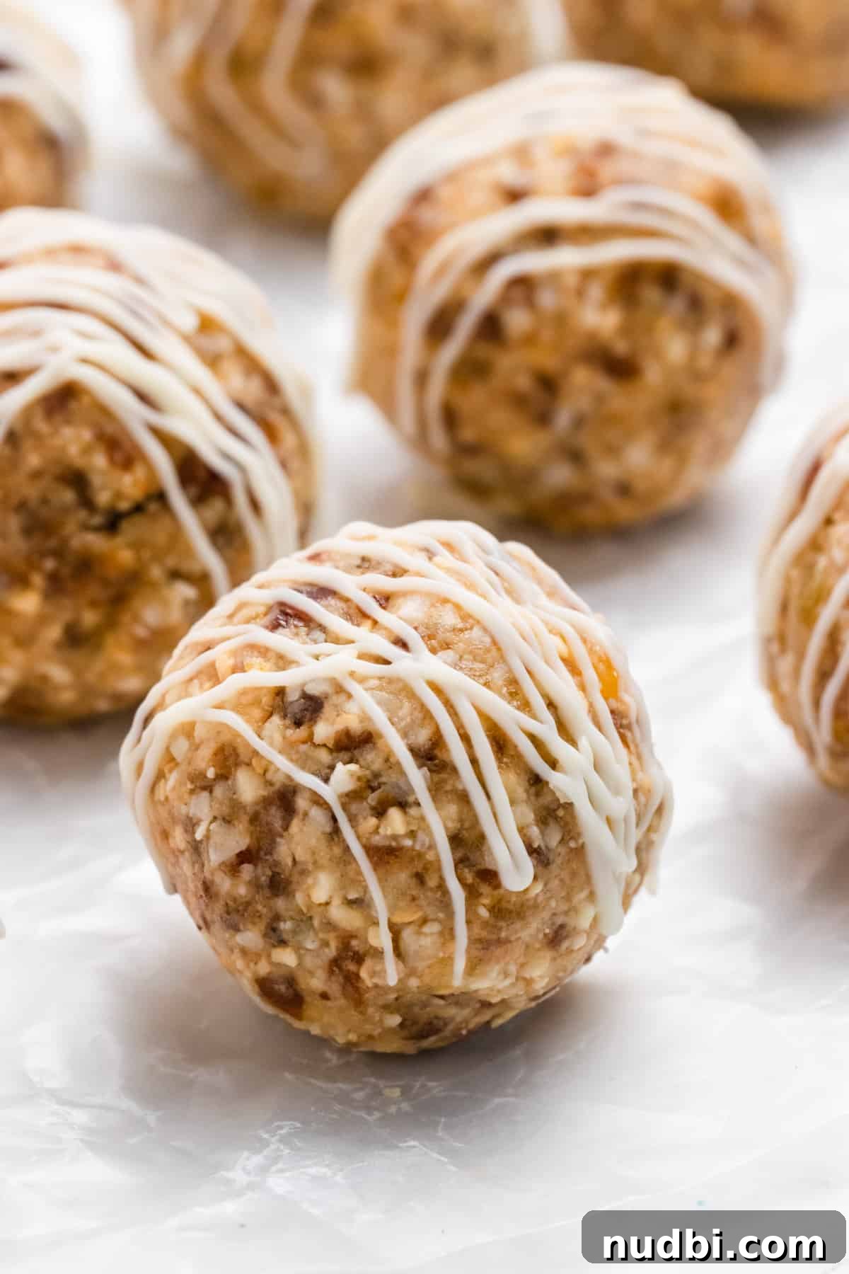 Coconut Mango Energy Bites: Tropical No-Bake Snack Recipe 2 Energy bites on parchment with white chocolate drizzle.