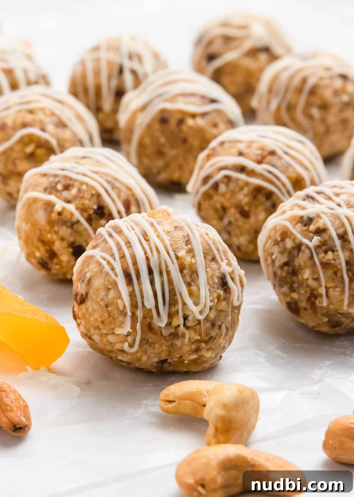 Coconut Mango Energy Bites: Tropical No-Bake Snack Recipe 6 Mango bites on parchment with cashews and drizzle.
