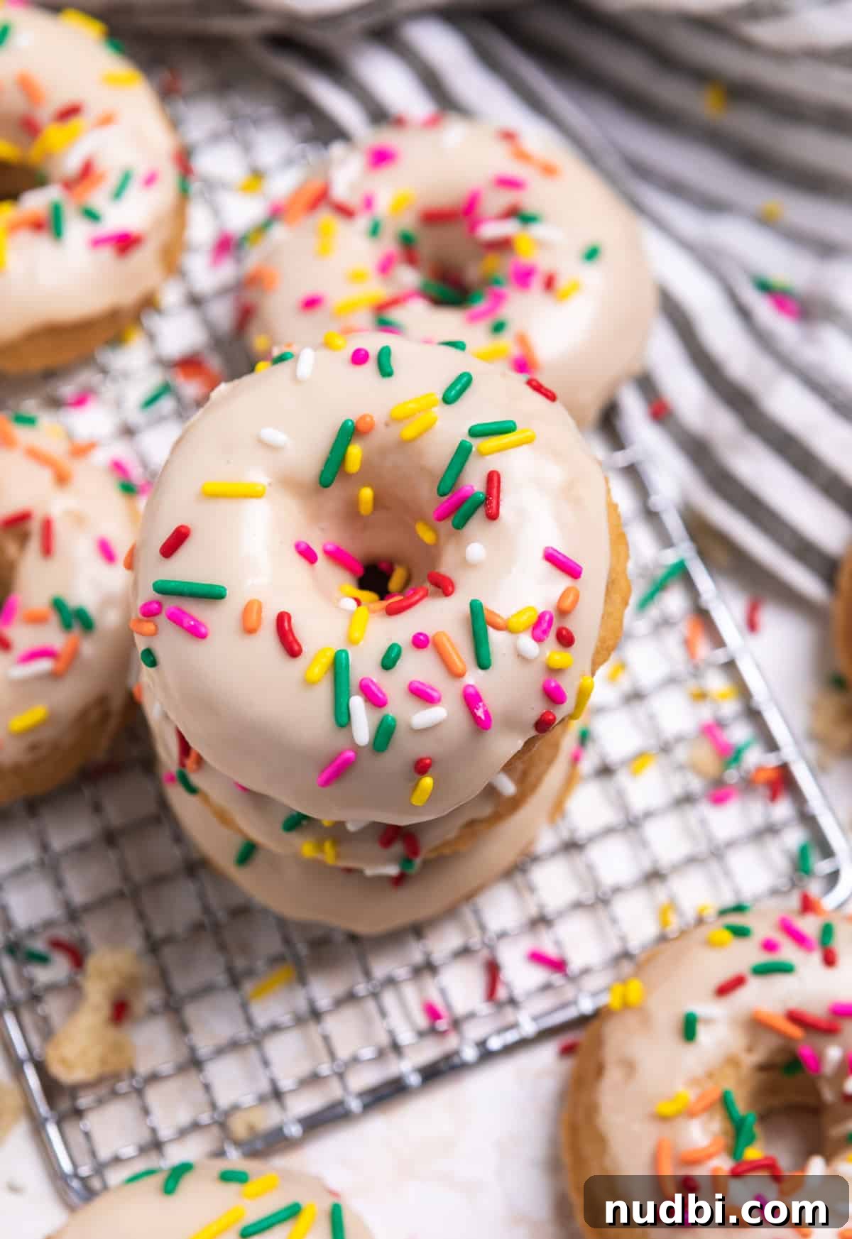 Triple Vanilla Donuts Recipe: Soft, Fluffy, and Extra Vanilla 2 Stack of vanilla donuts with icing and rainbow sprinkles.