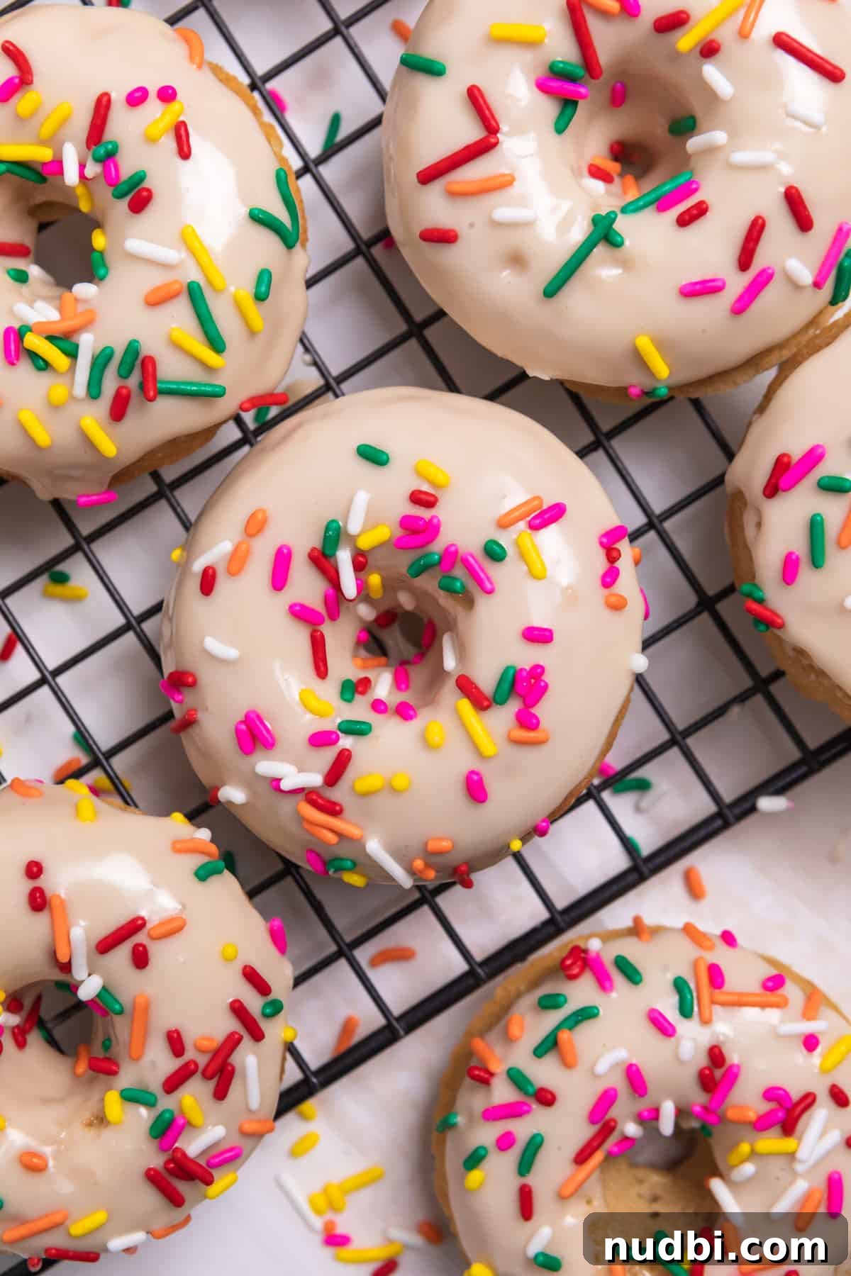 Triple Vanilla Donuts Recipe: Soft, Fluffy, and Extra Vanilla 8 Vanilla donuts with maple glaze and rainbow sprinkles on cooling rack.