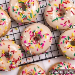 Triple Vanilla Donuts Recipe: Soft, Fluffy, and Extra Vanilla 9 Vanilla baked donuts with maple glaze and rainbow sprinkles on cooling rack.