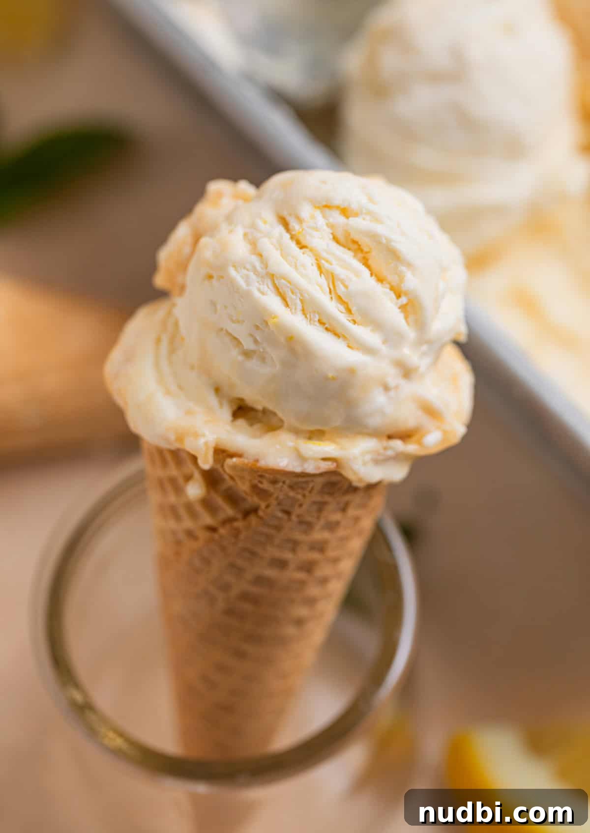 No-Churn Lemon Ice Cream Recipe — Creamy, Tart & Refreshing 12 Sugar ice cream cone topped with no churn lemon ice cream propped up in glass.