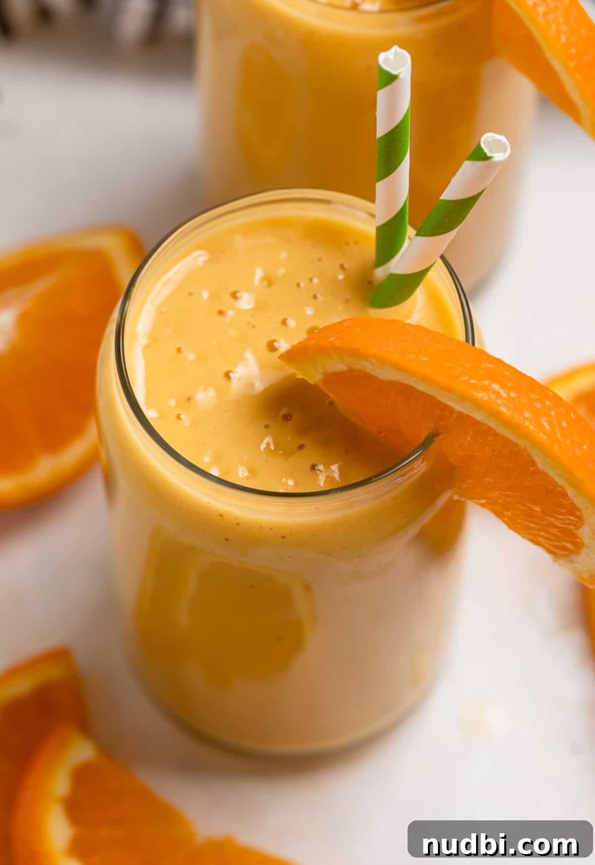 Orange Creamsicle Protein Smoothie Recipe for Creamy Vitamin C Boost 2 Orange banana smoothie in glass with orange slice garnish and striped straws.
