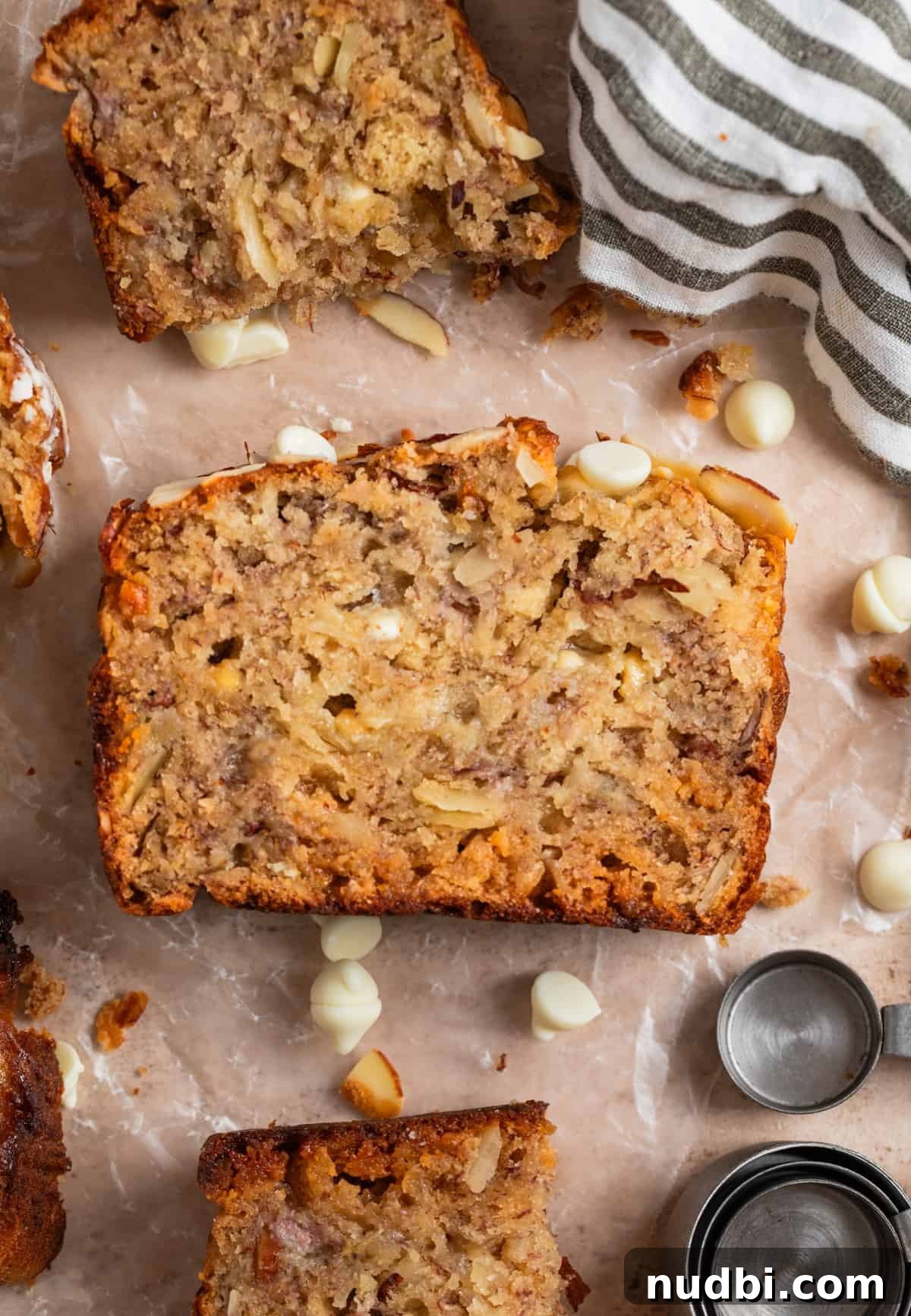 White Chocolate and Almond Banana Bread Recipe 2 White chocolate chip banana bread with sliced almonds on parchment with white chocolate chips surrounding.
