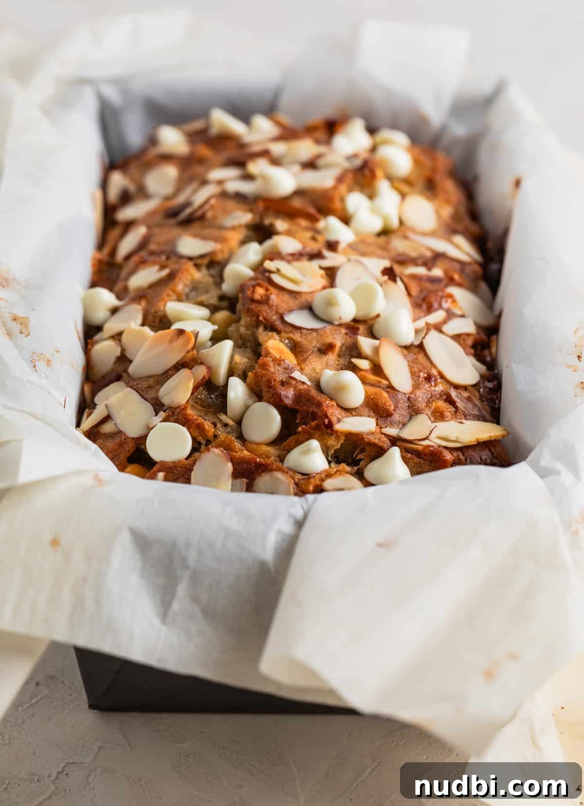 White Chocolate and Almond Banana Bread Recipe 7 Baked white chocolate chip and almond banana bread in pan with parchment.