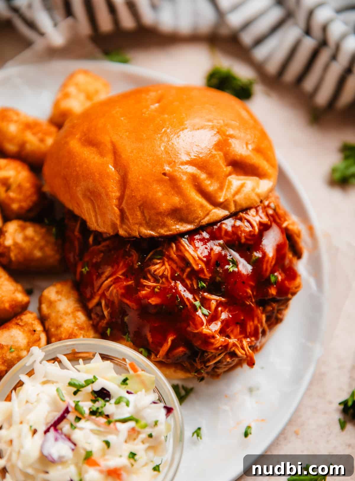Slow Cooker BBQ Shredded Chicken Recipe for Sandwiches and Tacos 2 Crock pot shredded BBQ chicken served on Brioche bun with extra BBQ sauce and cole slaw and tater tots.