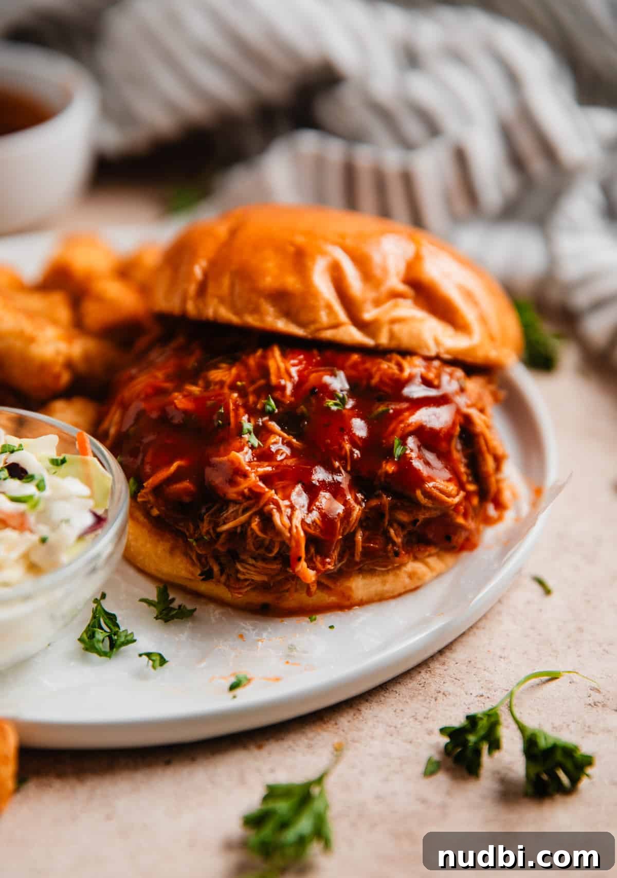 Slow Cooker BBQ Shredded Chicken Recipe for Sandwiches and Tacos 8 Pulled BBQ chicken sandwich on plate with cole slaw and tater tots.