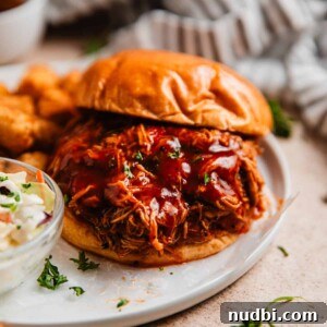 Slow Cooker BBQ Shredded Chicken Recipe for Sandwiches and Tacos 9 Brioche bun with pulled barbecue chicken and chopped parsley on white plate.