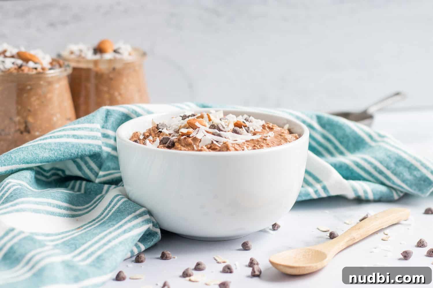 Almond Joy Overnight Oats Recipe — Chocolate, Coconut & Almonds 2 White bowl with almond joy overnight oats and jars in background.