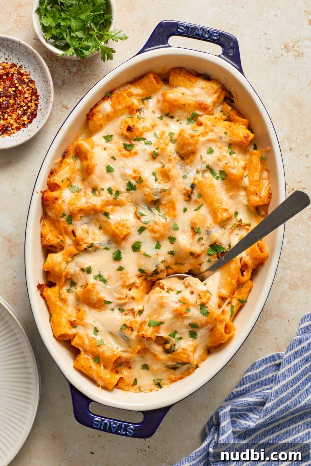 Creamy Pumpkin Ricotta Pasta Bake with Parmesan Crisp Topping 2 Pumpkin Pasta bake in casserole dish topped with melted cheese and chopped parsley with serving spoon scooping in.