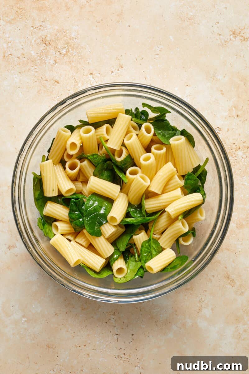 Creamy Pumpkin Ricotta Pasta Bake with Parmesan Crisp Topping 6 Rigatoni and spinach in glass mixing bowl.