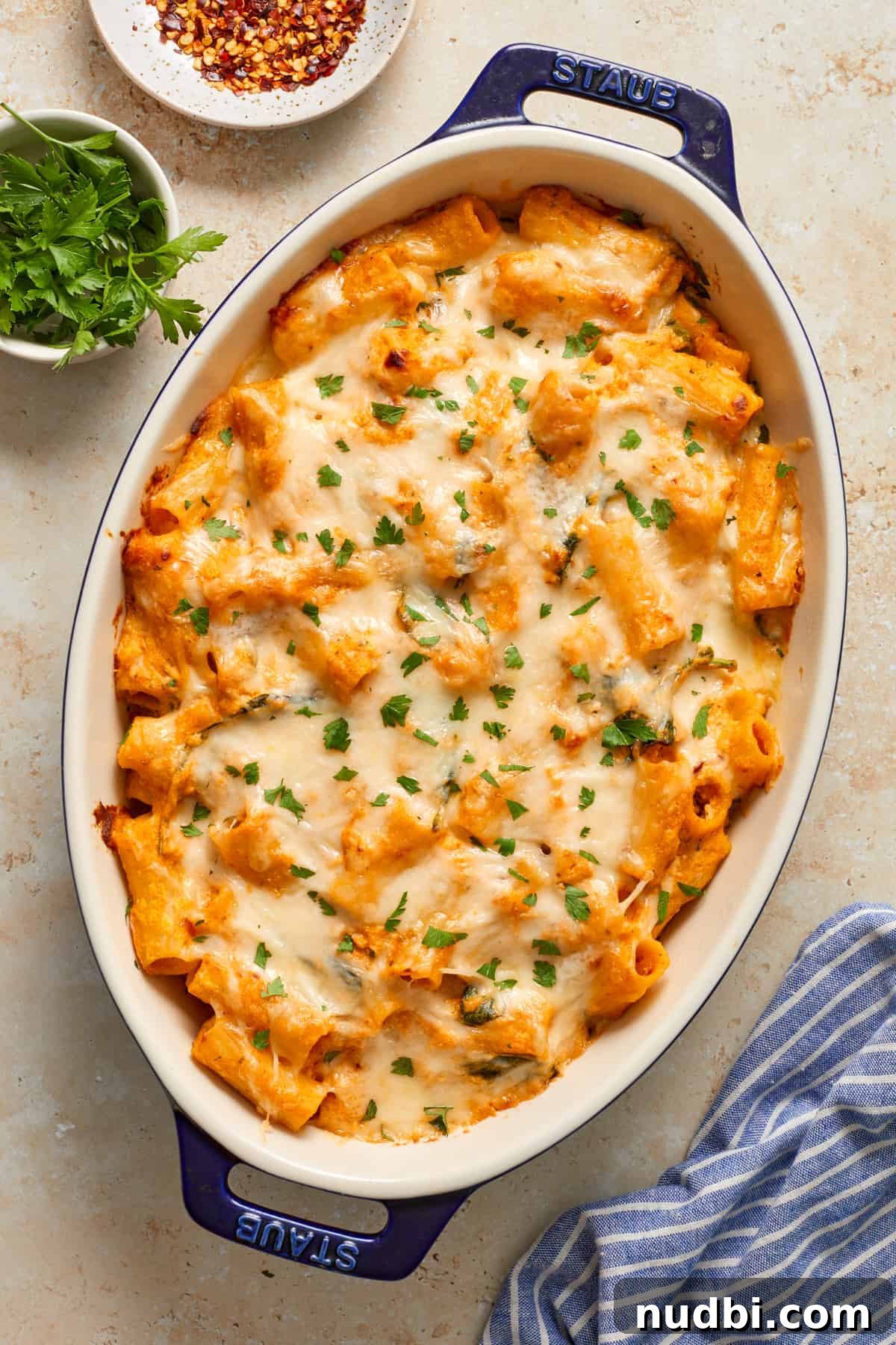 Creamy Pumpkin Ricotta Pasta Bake with Parmesan Crisp Topping 9 Baked pumpkin pasta in blue pan with cheese melted on top and chopped parsley.