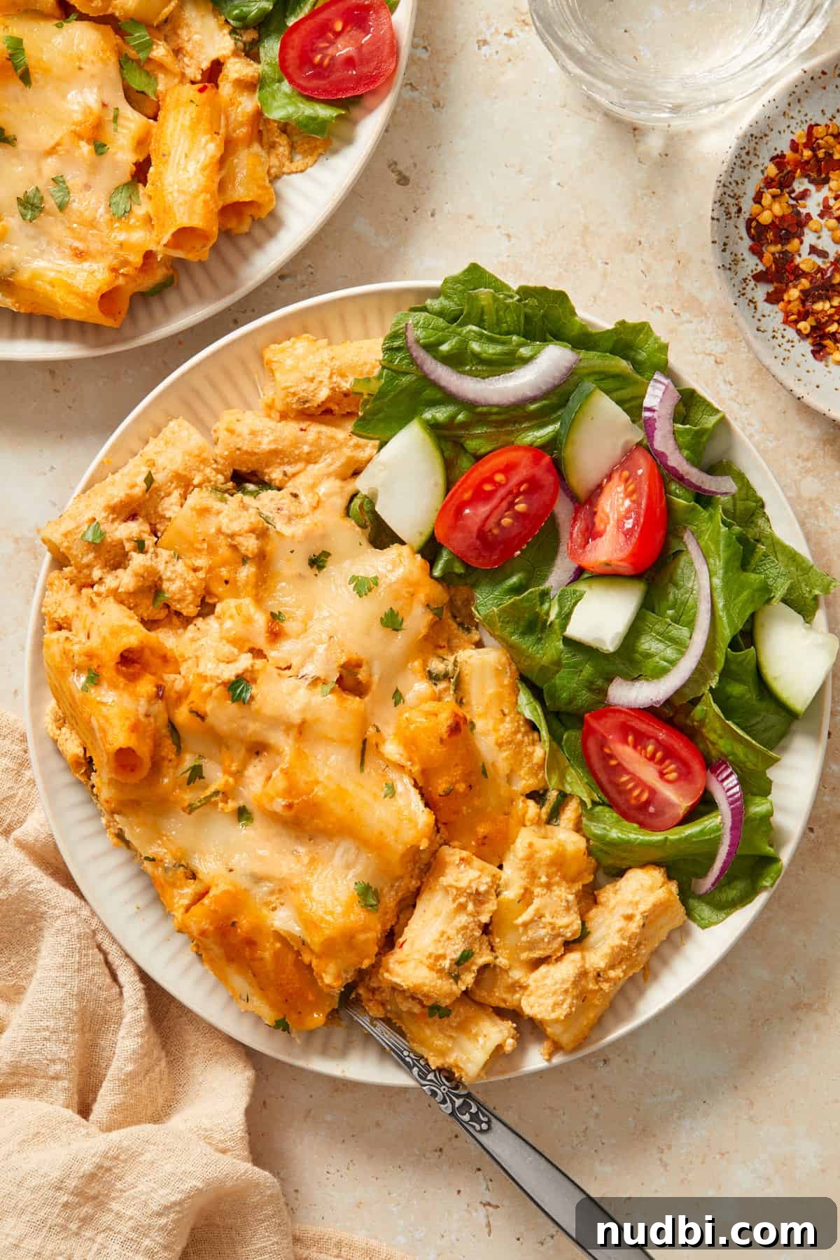 Creamy Pumpkin Ricotta Pasta Bake with Parmesan Crisp Topping 10 White plate with baked pumpkin pasta and salad with tomato, cucumber and onion.