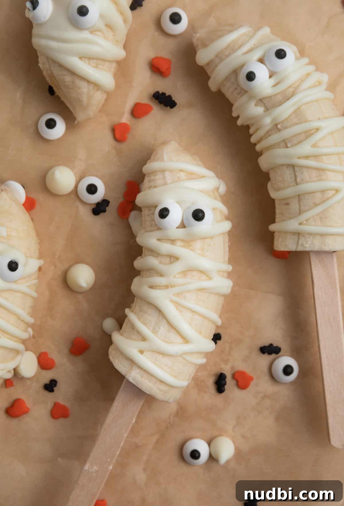 Spooky Banana Mummy Pops: Halloween Treats for Kids 2 Banana mummy pops with candy eye balls on parchment.