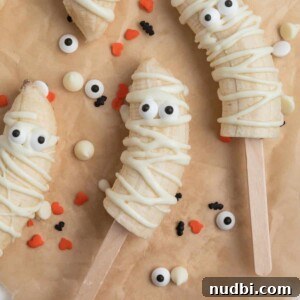Spooky Banana Mummy Pops: Halloween Treats for Kids 5 Mummy banana pops with candy eyeballs on parchment.