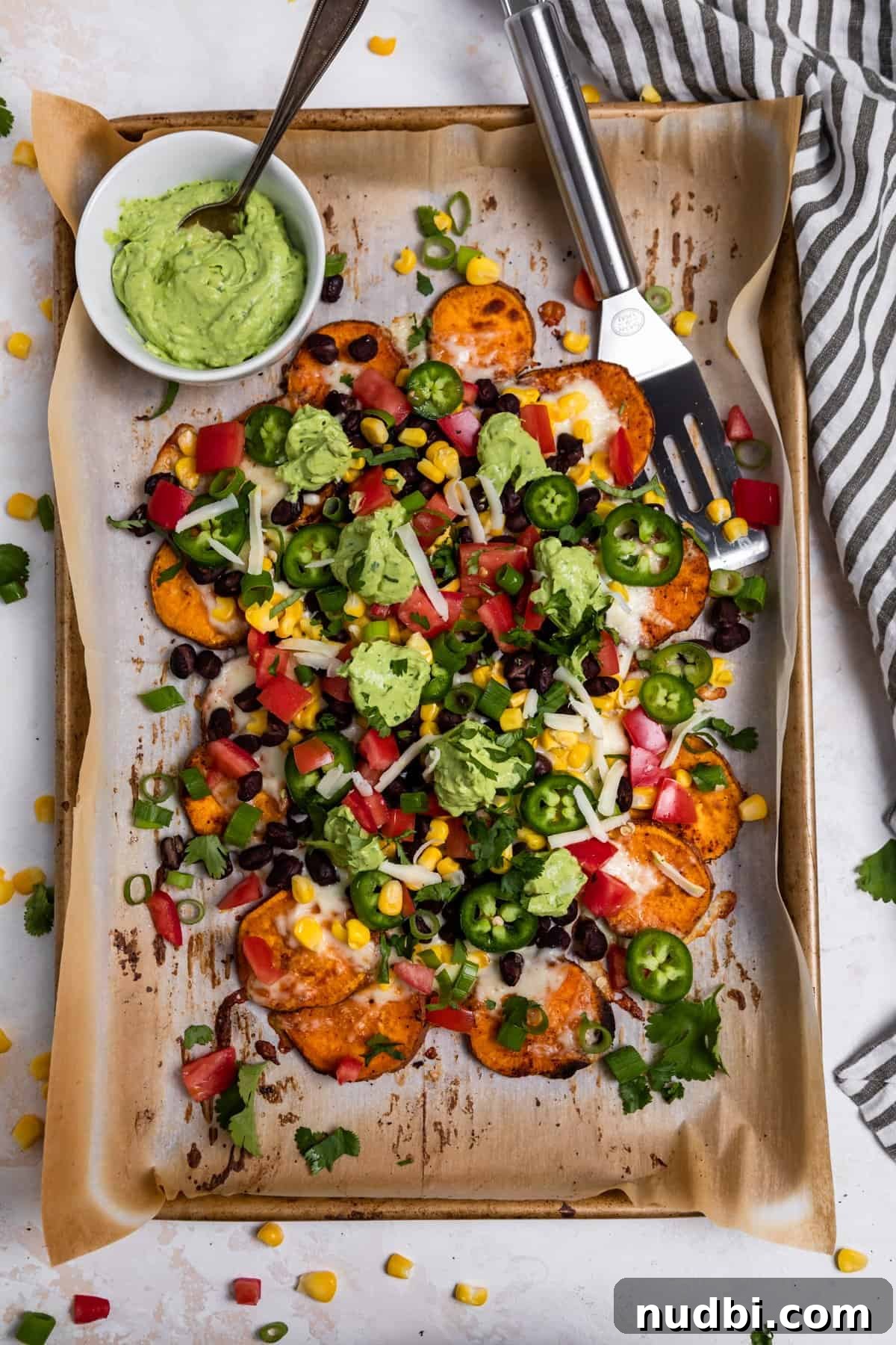 Sweet Potato Nachos with Creamy Avocado Sauce 9 Overhead view of sheetpan with loaded sweet potato nachos and bowl of avocado crema.