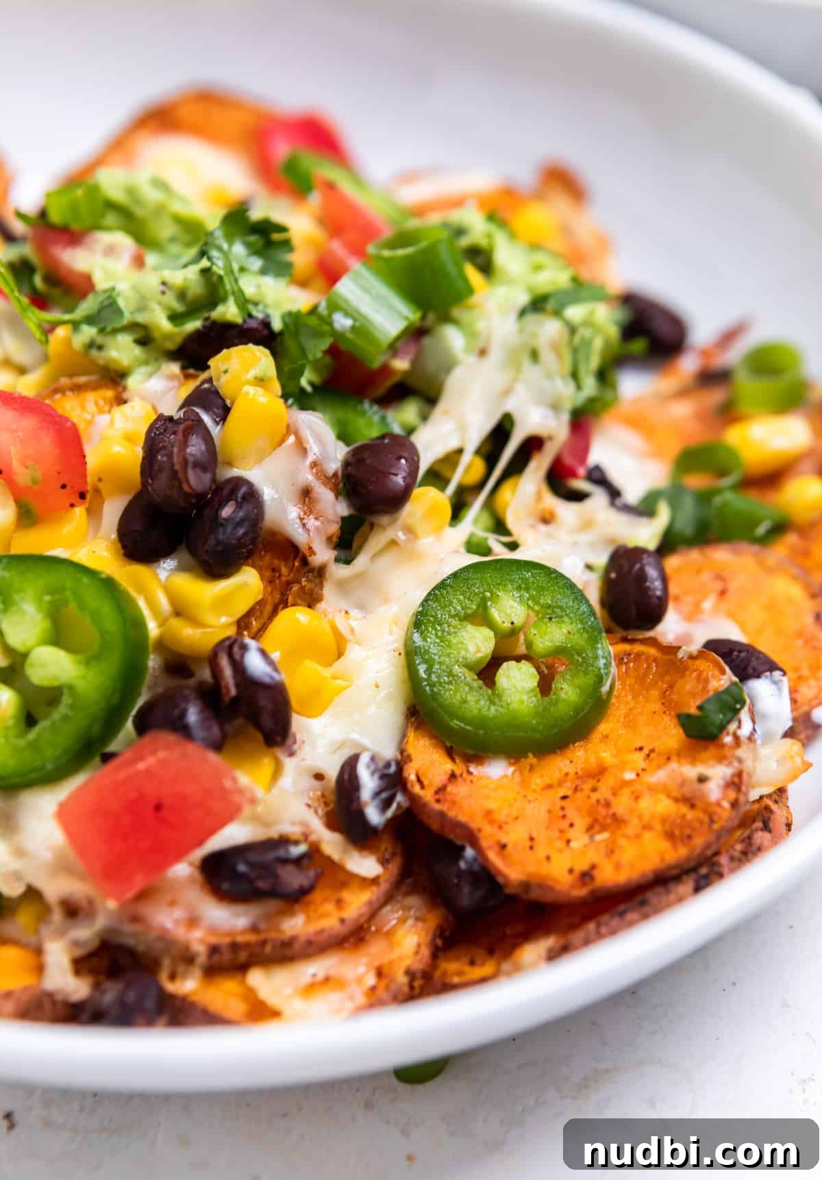 Sweet Potato Nachos with Creamy Avocado Sauce 10 White bowl with sweet potatoes topped with corn, cheese, beans and other ingredients.