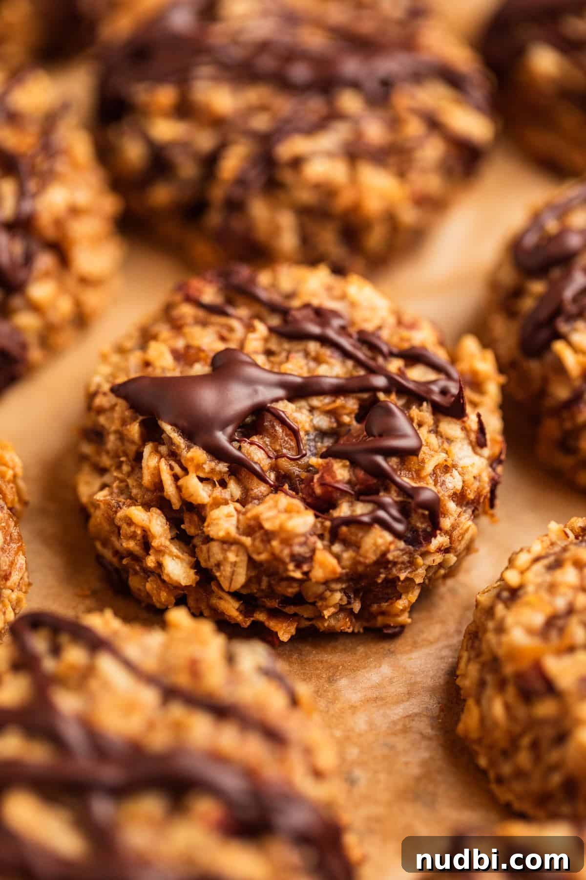 Peanut Butter Banana Oatmeal Breakfast Cookies That Keep You Full 2 Oatmeal cookies with peanut butter and banana on parchment with chocolate drizzle over top.