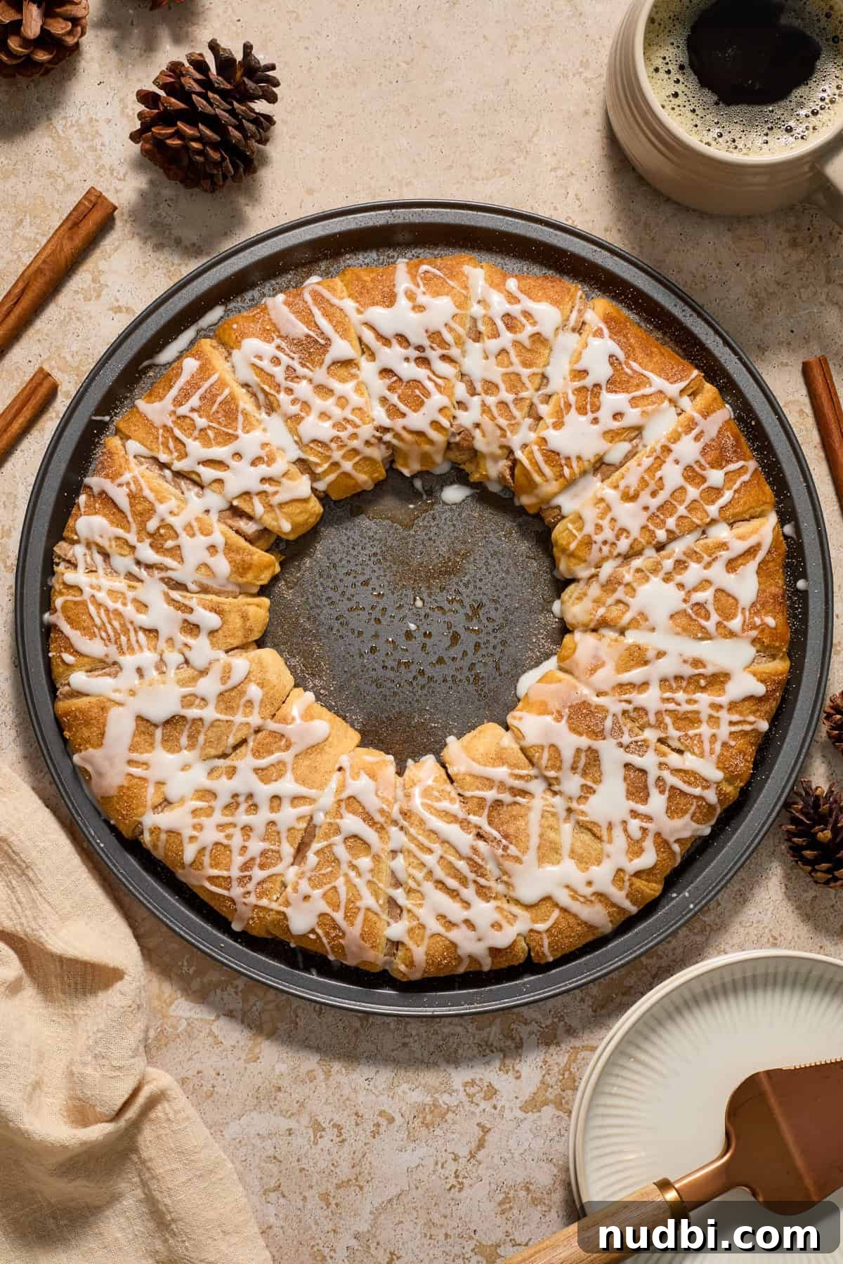 Cinnamon Crescent Roll Wreath Recipe — Festive Holiday Pastry 2 Cinnamon crescent roll wreath on pan with coffee and cinnamon sticks surrounding.