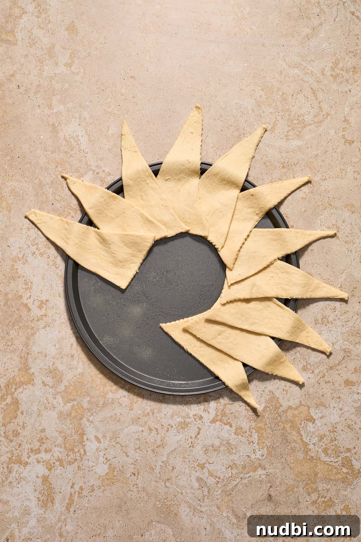 Cinnamon Crescent Roll Wreath Recipe — Festive Holiday Pastry 6 Crescent dough lined over halfway around a pizza pan to form a circular wreath shape.