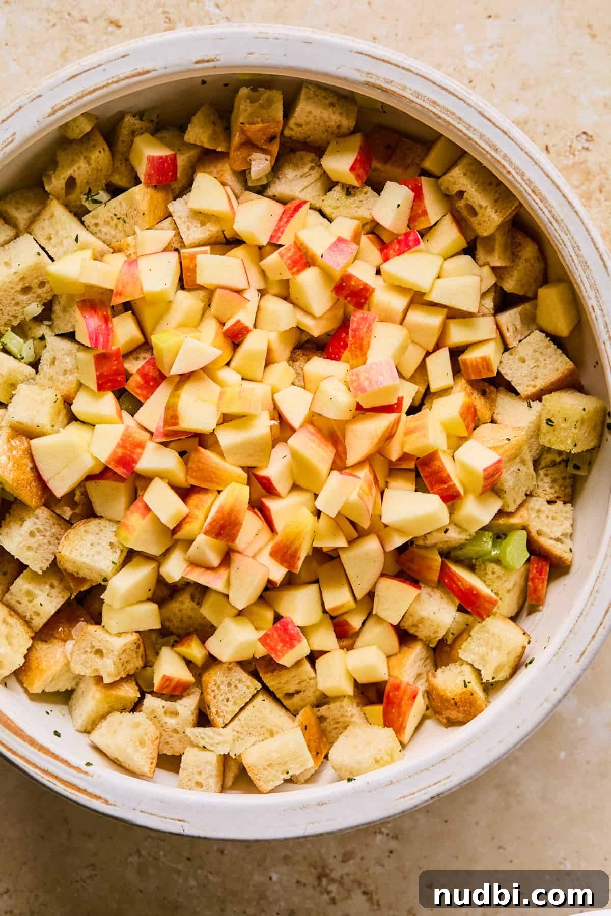 Apple and Sage Stuffing with Cranberries and Pecans 7 Celery and onion mixture added to mixing bowl with chopped apples added on top.