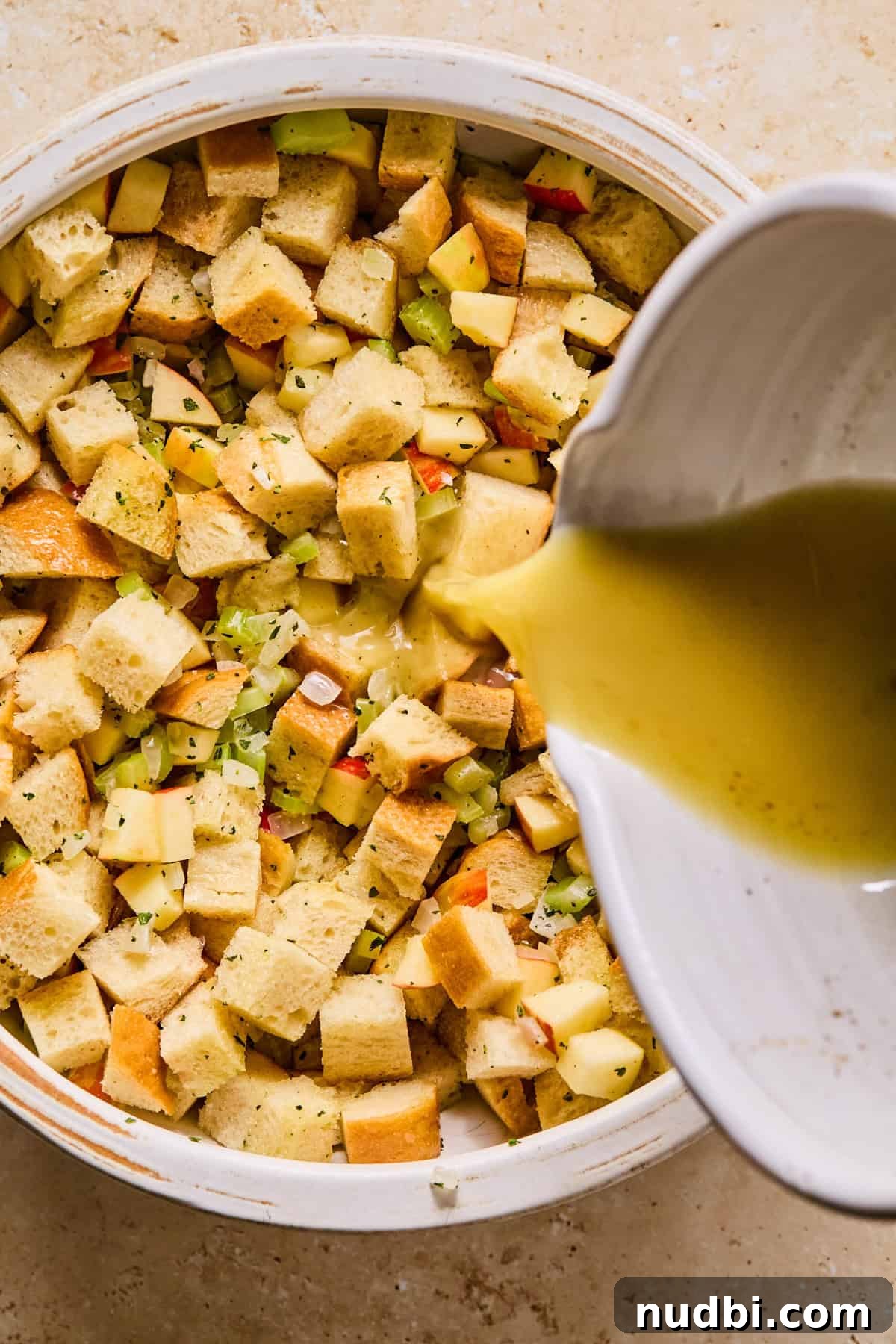 Apple and Sage Stuffing with Cranberries and Pecans 9 Broth mixture added to bowl with apple stuffing ingredients.