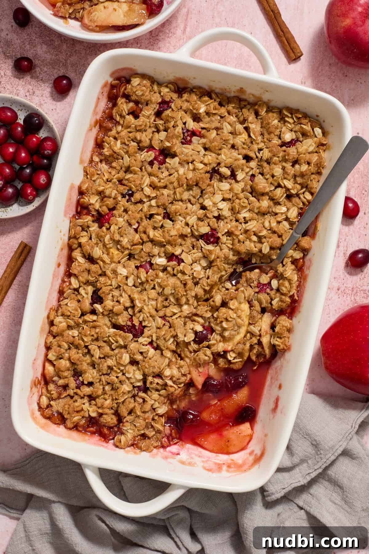 Cranberry Apple Crisp Recipe — Tart & Spiced Autumn Dessert 7 White baking pan with cranberry apple crisp with serving spoon scooping into the dessert.