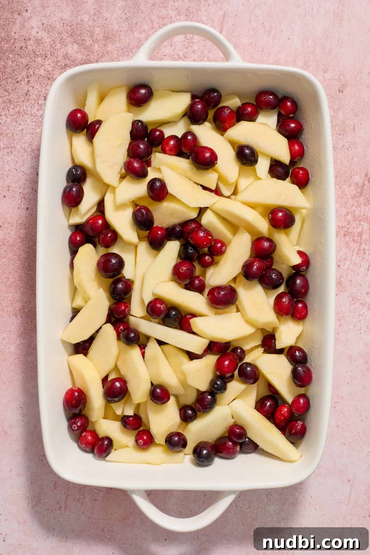 Cranberry Apple Crisp Recipe — Tart & Spiced Autumn Dessert 4 Cranberries and apples in white baking dish.