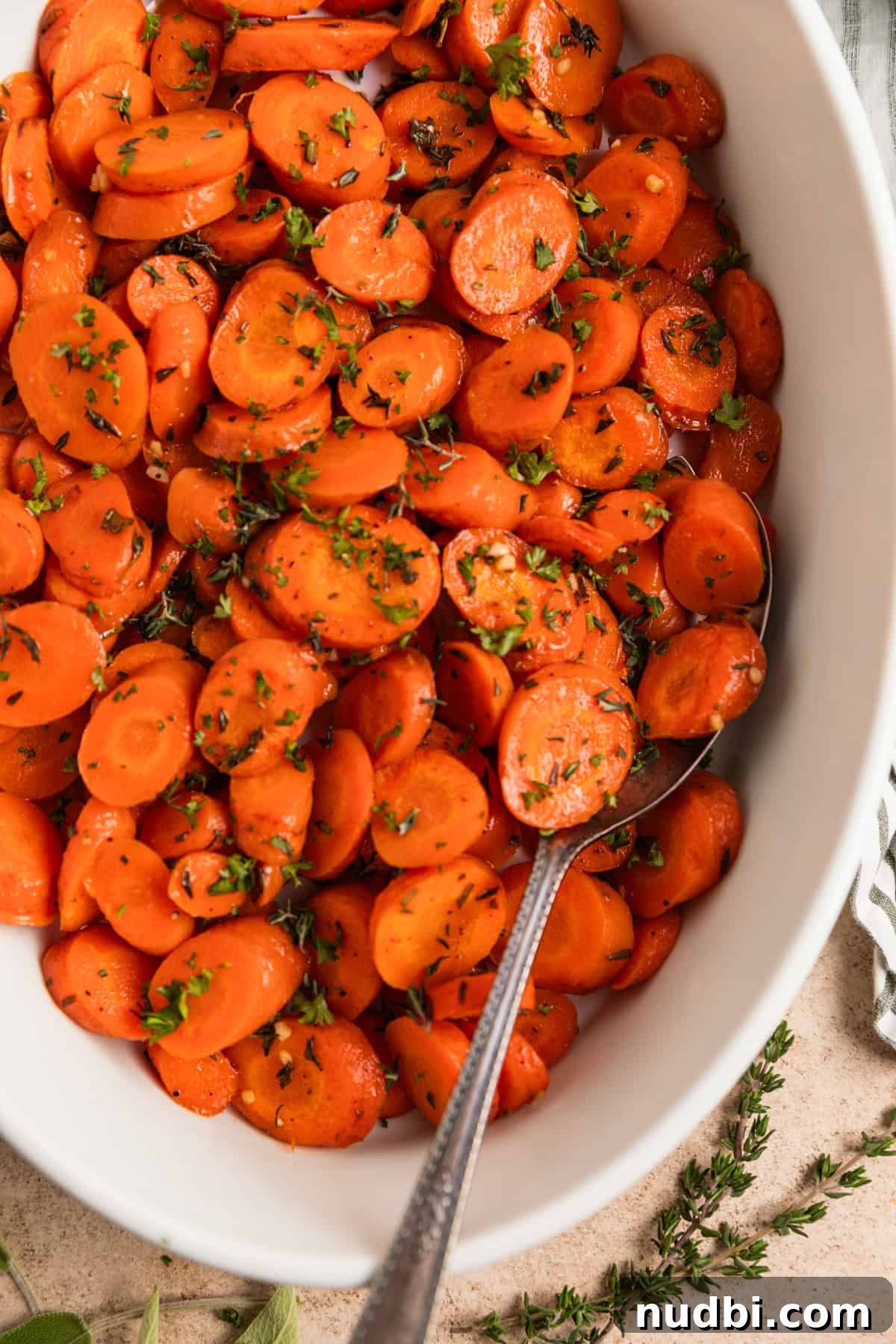 Maple-Glazed Herb-Roasted Carrots with Garlic and Thyme 2 Maple glazed herbed carrots with fresh herbs in white dish with serving spoon.