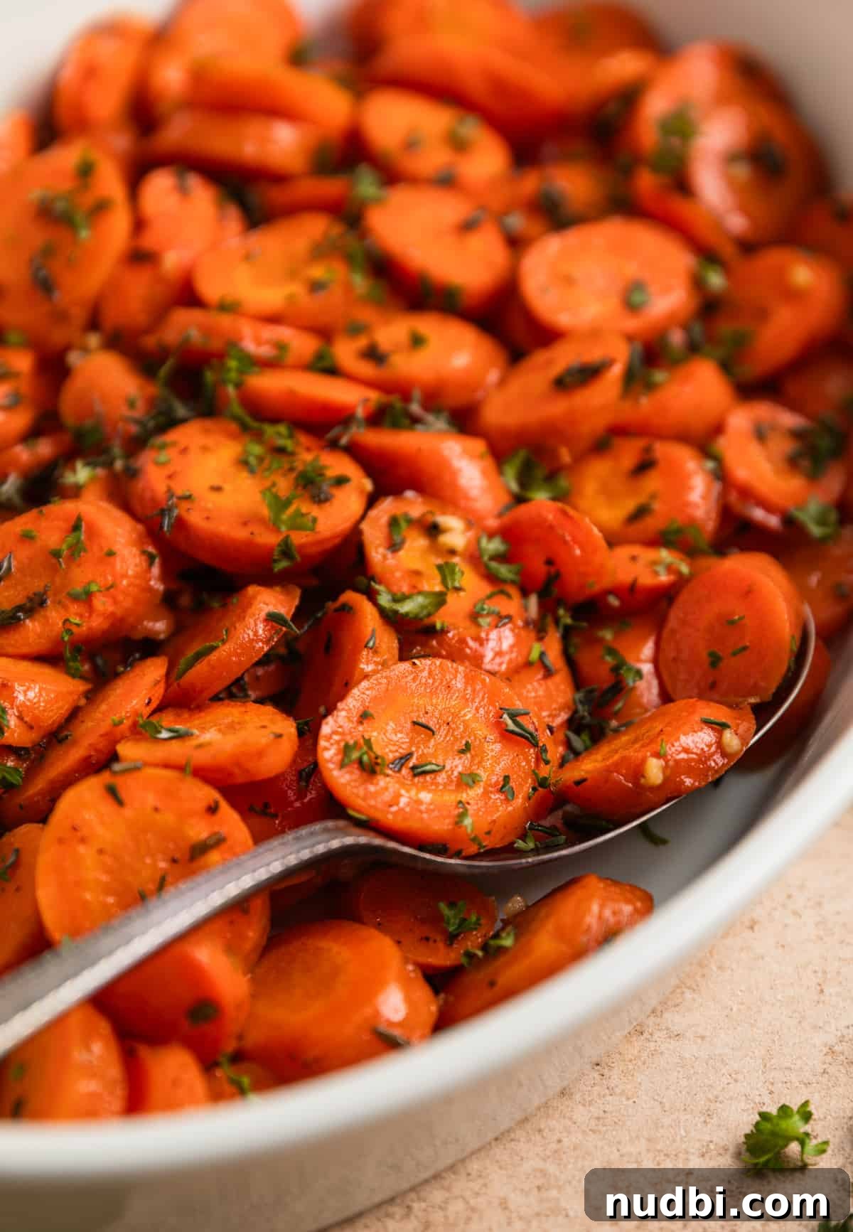 Maple-Glazed Herb-Roasted Carrots with Garlic and Thyme 3 Roasted carrots in white bowl with serving spoon.