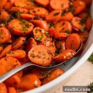 Maple-Glazed Herb-Roasted Carrots with Garlic and Thyme 5 Serving spoon scooping into carrots in white dish.