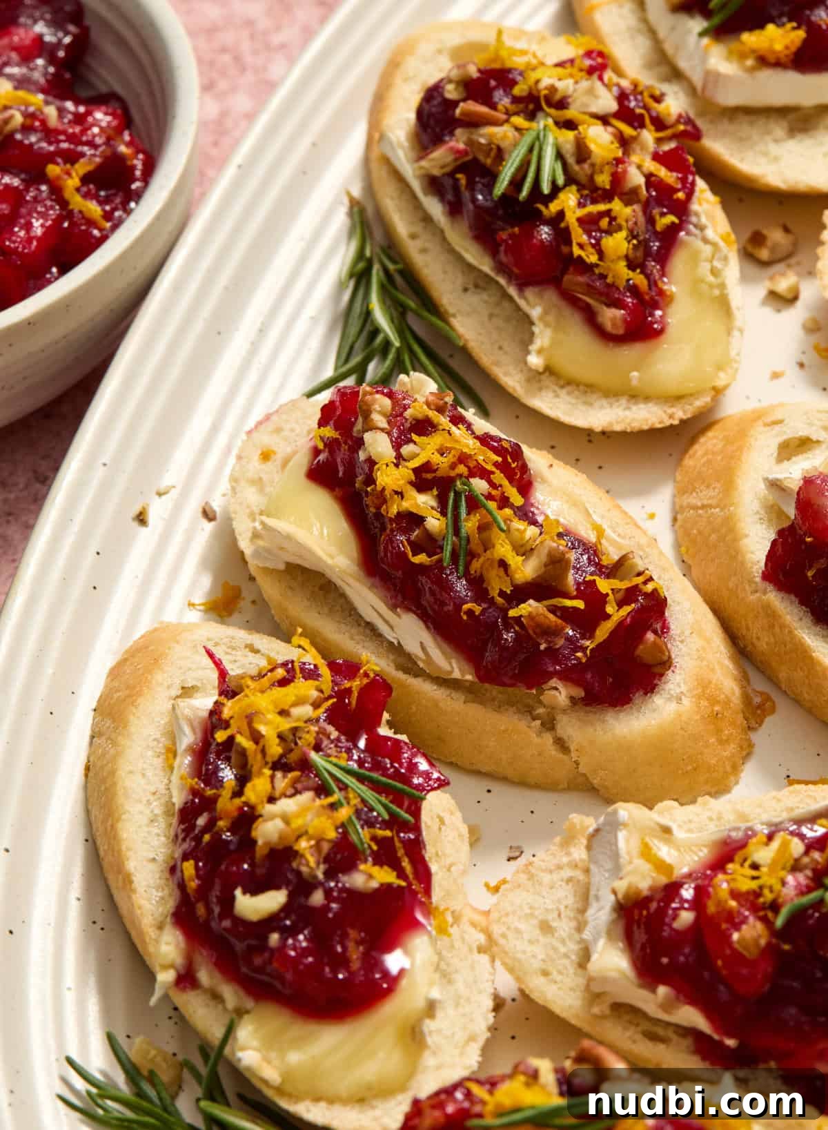 Cranberry Brie Crostini Recipe for Holiday Appetizers 2 Crostini on serving dish topped with brie and cranberry sauce.