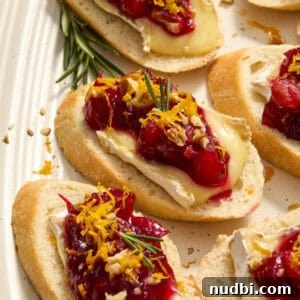 Cranberry Brie Crostini Recipe for Holiday Appetizers 11 Cranberry topped brie crostini on plate topped with fresh rosemary and orange zest.