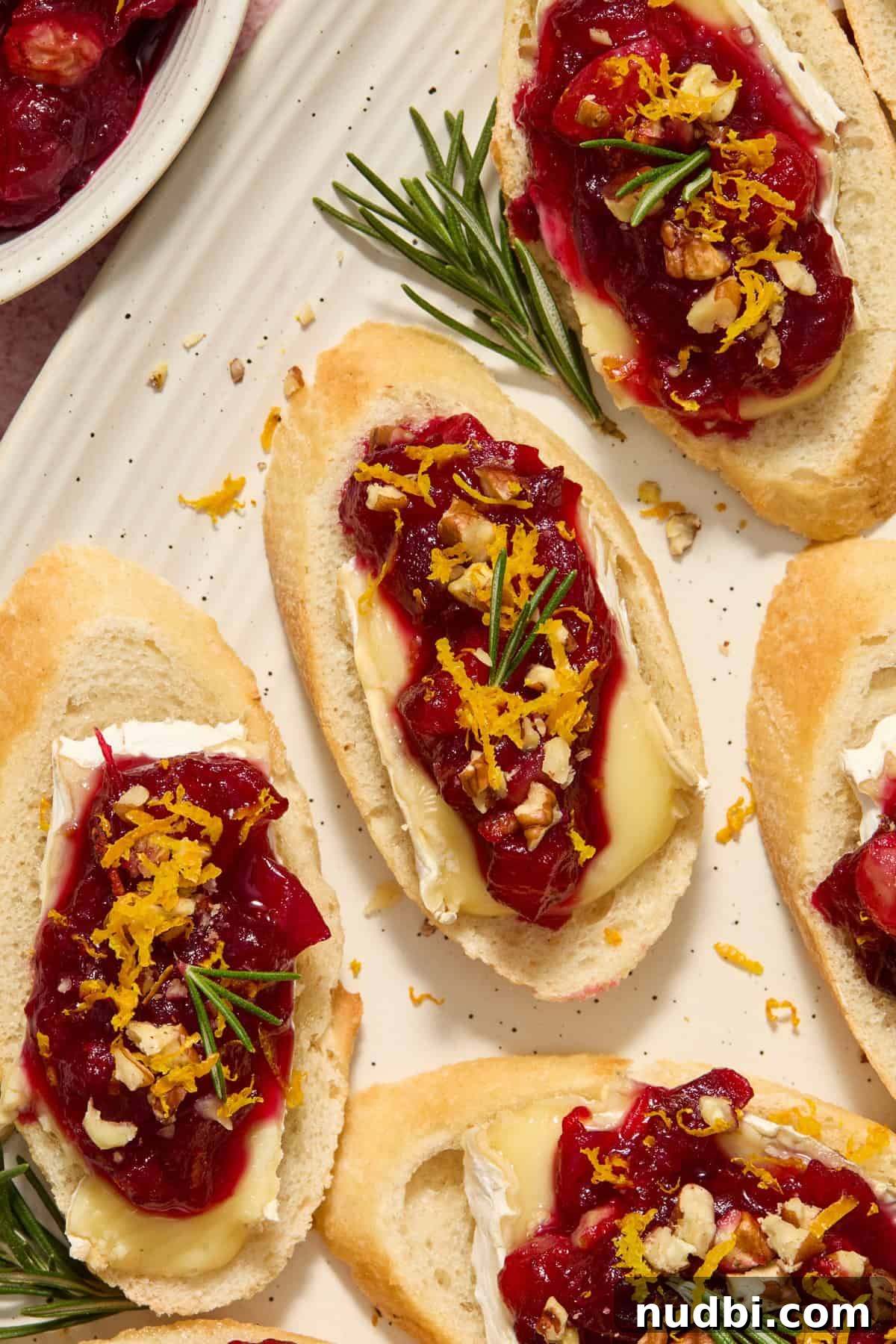 Cranberry Brie Crostini Recipe for Holiday Appetizers 3 Cranberry brie crostini on plate with fresh rosemary on top.