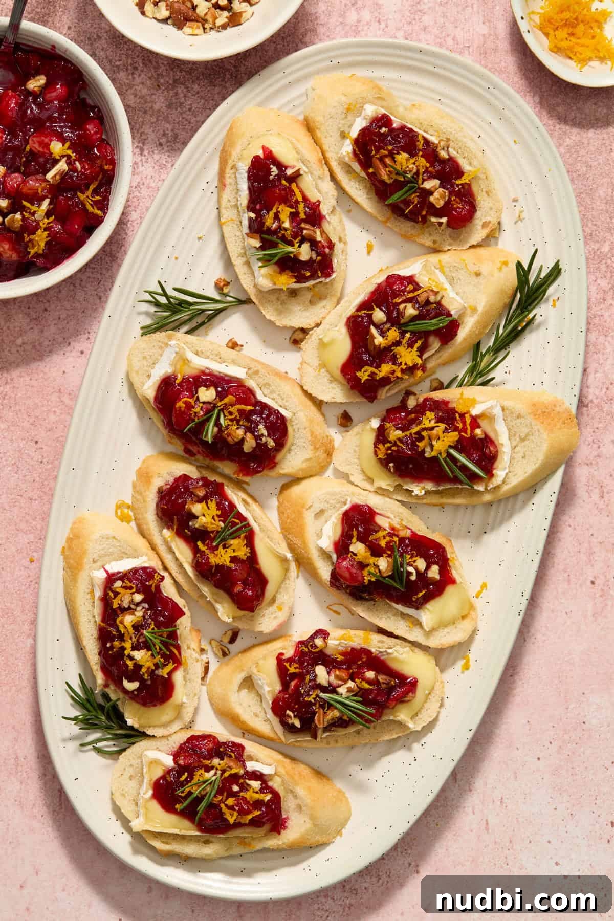 Cranberry Brie Crostini Recipe for Holiday Appetizers 10 Serving platter with cranberry brie crostini topped with fresh herbs and orange zest.